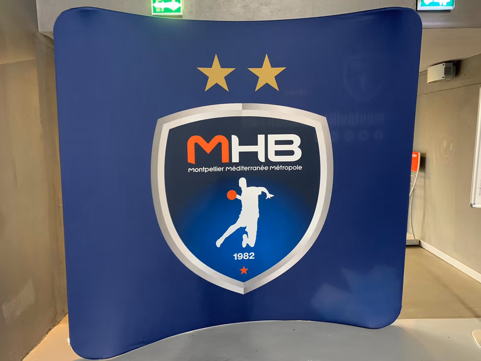 Mur d'interview courbe du Montpellier Handball (MHB) couvert de logos partenaires en conférence de presse